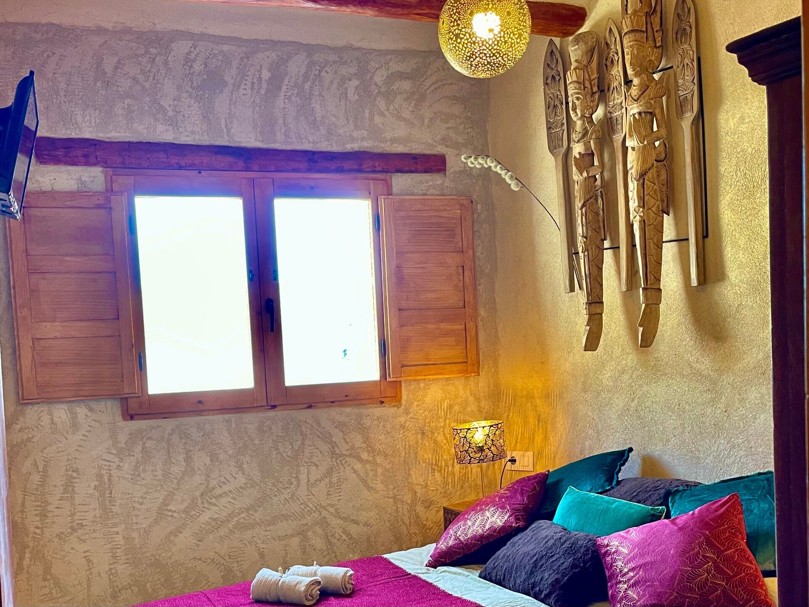Ein Zimmer mit Holzhörnern, einem Bett mit bunten Kissen, einer Wandskulptur und einer Hängeleuchte.