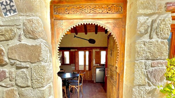 Um corredor com paredes de pedra que leva a uma sala de jantar com mesa e cadeiras, e uma cozinha ao fundo.