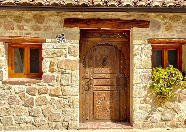A stone building with a wooden door, two windows, and a small plant.
