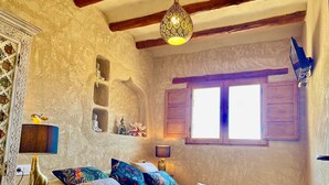 Quarto com cama, almofadas, luminária, estátua de Buda, janela e luminária pendente.
