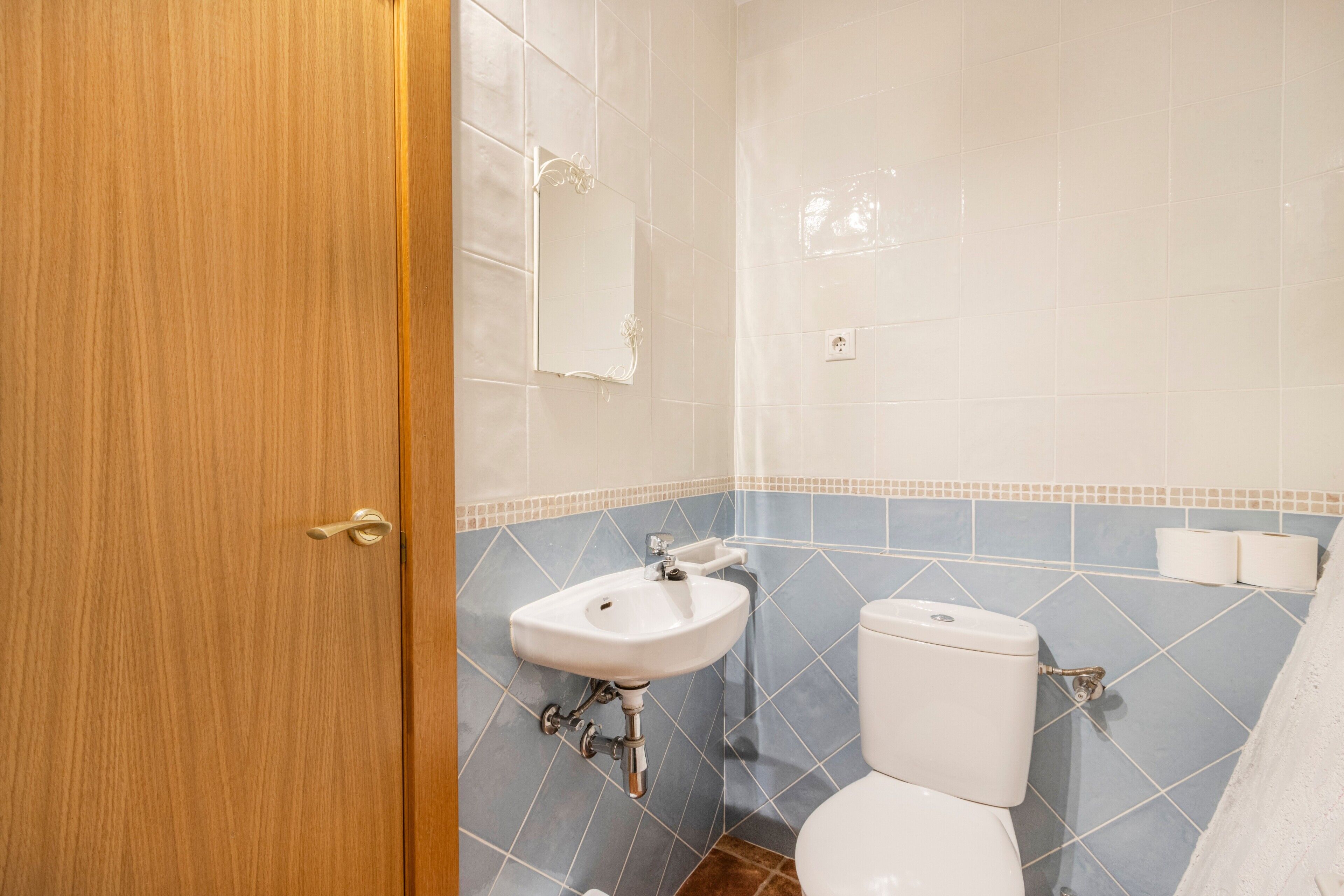 A bathroom with a wooden door, a white sink, a toilet, and blue-tiled walls.