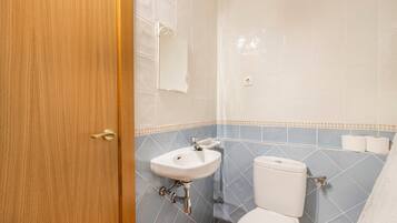 A bathroom with a wooden door, a white sink, a toilet, and blue-tiled walls.