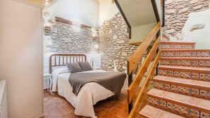 A bedroom with a bed, a wooden staircase, and stone walls. - Apartment 'El Pedregal' with Mountain View, Wi-Fi and Air Conditioning (Graus)