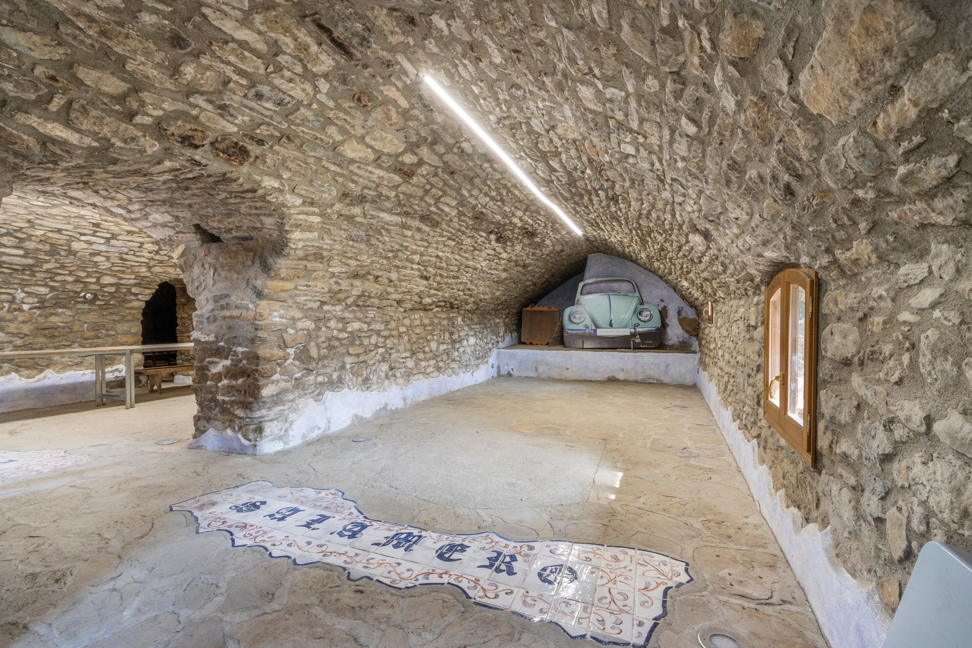 An interior with stone walls, a tiled floor with a map, a bench, and a window.