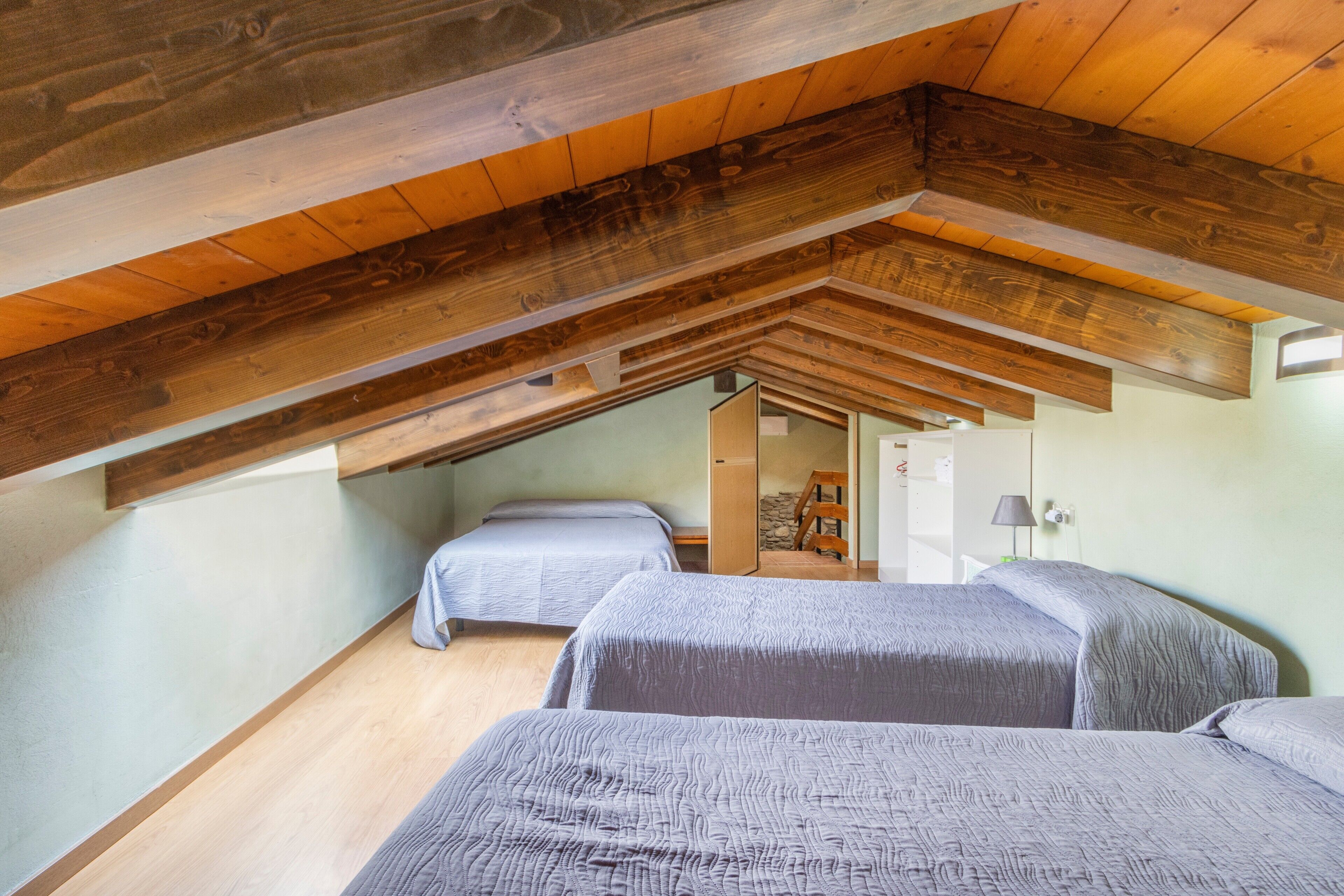 Een slaapkamer in loftstijl met houten balken, twee bedden en een trap naar een hoger niveau.