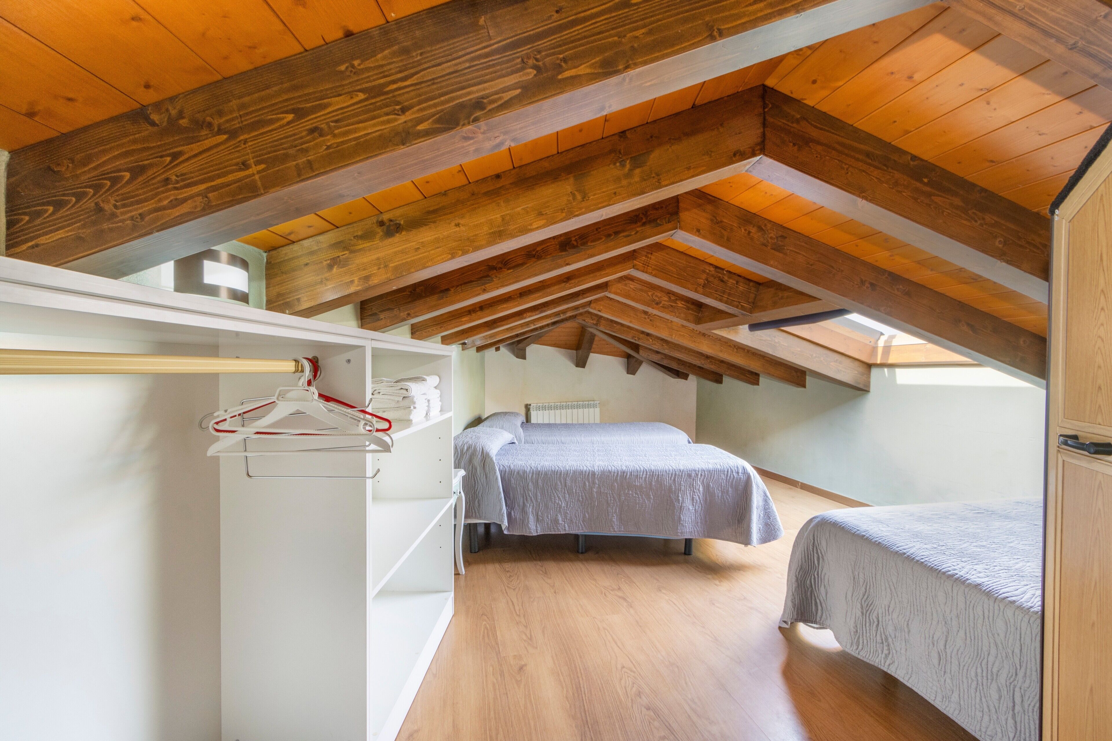 Une chambre avec un plafond en pente, des poutres apparentes, un lit, une table de chevet et un portant à vêtements.