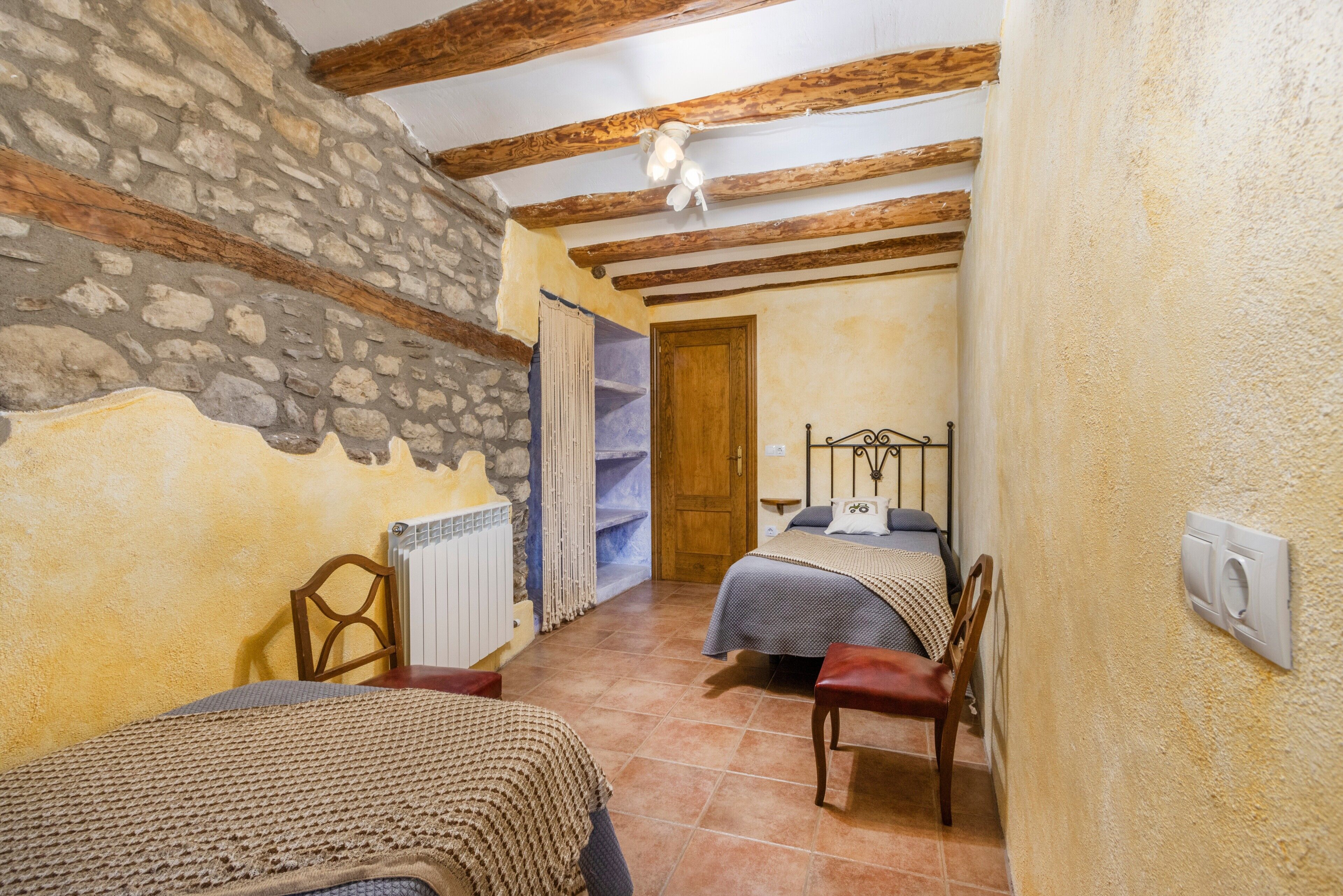 Une chambre avec des murs en pierre, des poutres en bois, un lit, une chaise et un radiateur.