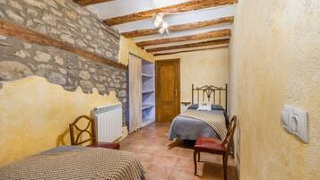 Une chambre avec des murs en pierre, des poutres en bois, un lit, une chaise et un radiateur.