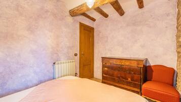 A bedroom with a wooden ceiling, a wooden dresser, a red chair, a bed with a white bedspread, and a radiator.