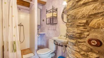 A bathroom with a shower, toilet, sink, and a stone wall.