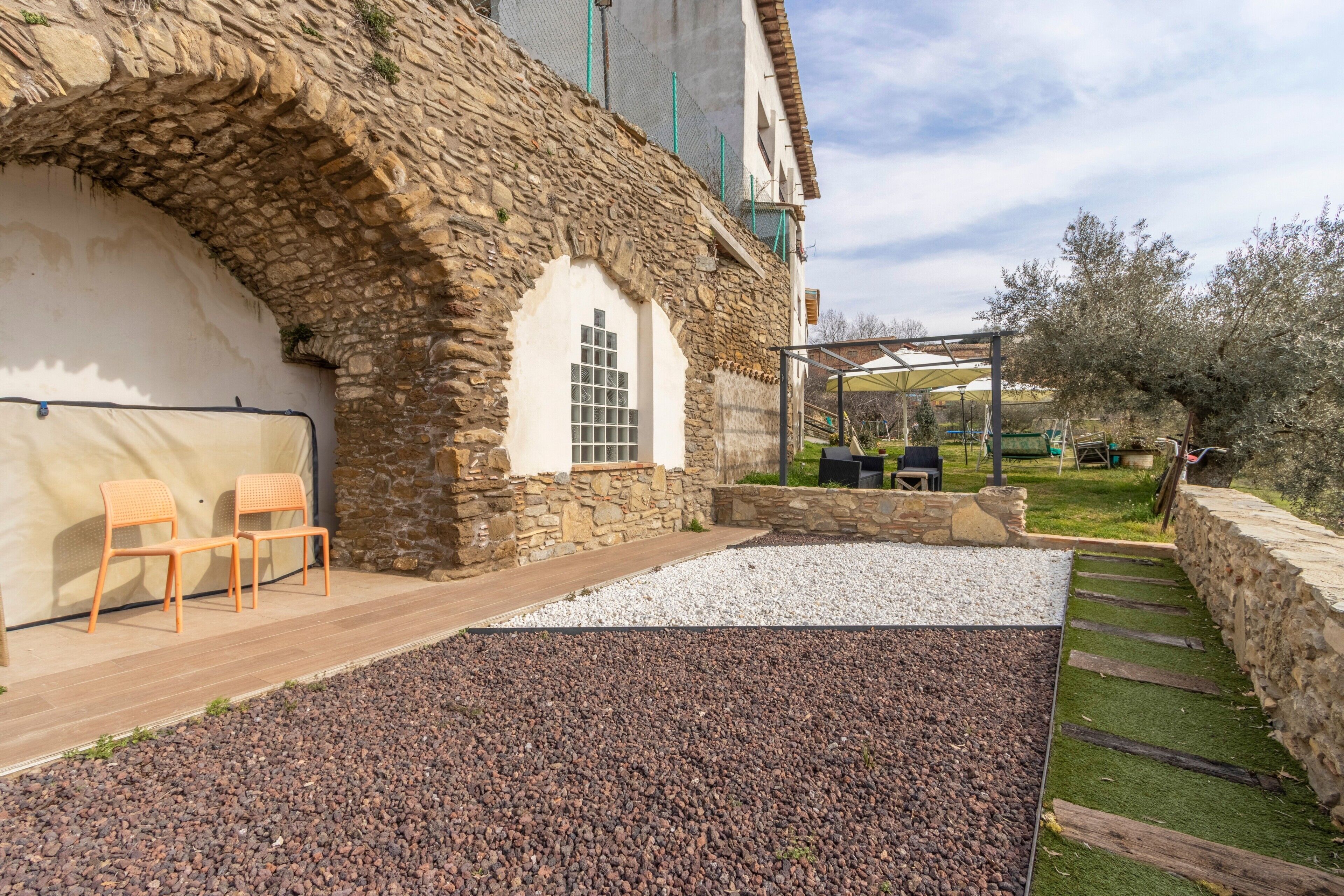 Un bâtiment en pierre avec un mur blanc, une terrasse en bois et des sièges extérieurs.