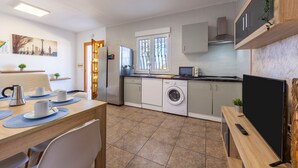 Eine moderne Küche mit Waschmaschine, eine Essecke mit Tisch für zwei Personen und ein Fernseher auf einem Holzboden.
