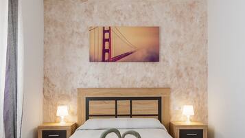 Une chambre d’hôtel avec un lit, deux tables de chevet avec des lampes, un tableau représentant le Golden Gate Bridge accroché au mur, et une décoration en forme de cœur sur le lit.