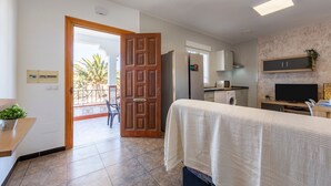 Ein Hotelzimmer mit Bett, Fernseher, Küchenzeile und Blick auf Palmen durch eine offene Tür.