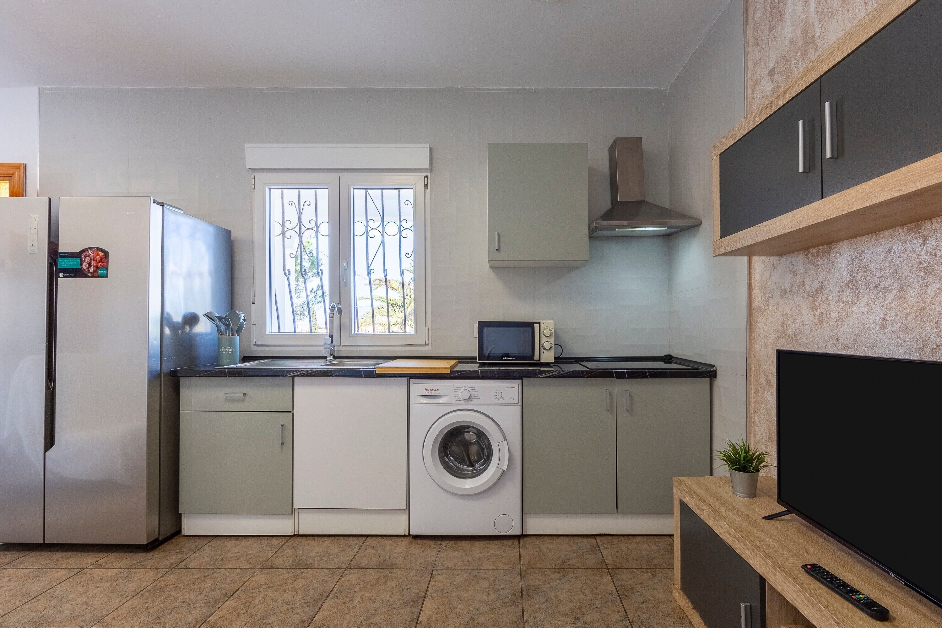 Una cocina moderna con lavadora, microondas y televisor.