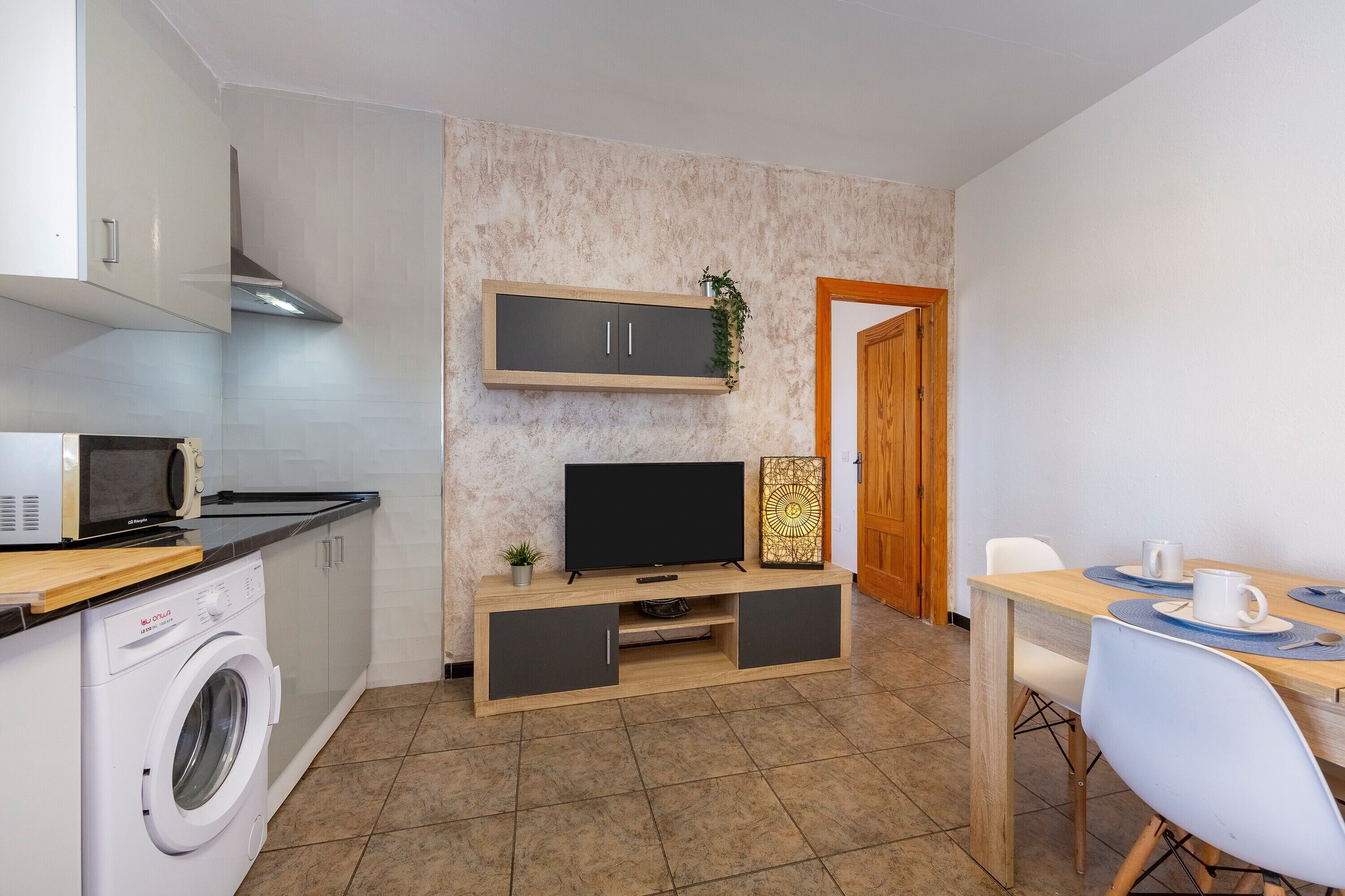A compact kitchen with a washing machine, microwave, and a TV on a wooden cabinet.
