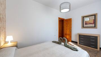 A bedroom with a bed, a bedside lamp, a dresser, a door, and a framed picture on the wall.