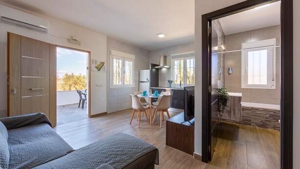 A modern room with a bed, a dining table with chairs, a kitchen area, and a balcony with a view. - Apartment 'Citronela' with Private Terrace and Air Conditioning (Nijar)