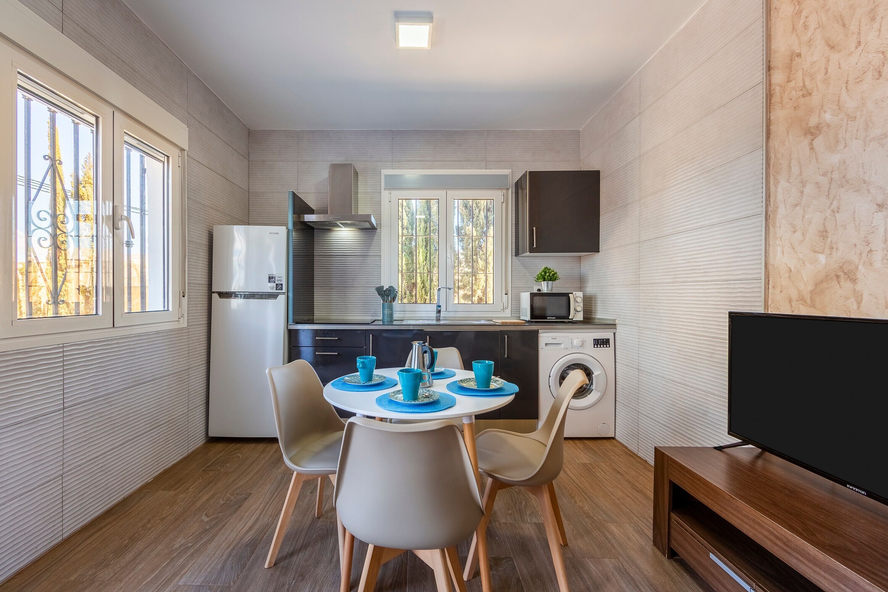 Una cocina compacta con zona de comedor, lavadora y televisor de pantalla plana.