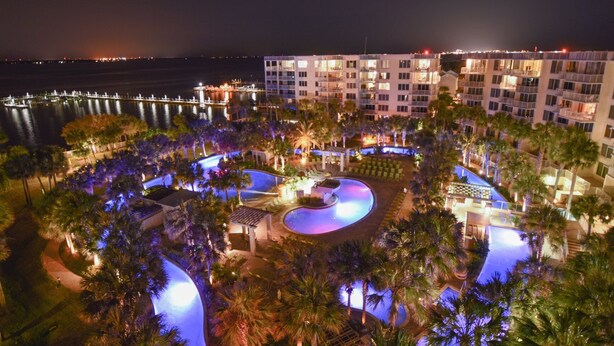 Een resort met meerdere zwembaden, palmbomen en uitzicht op het water.