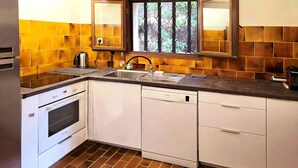 A compact kitchen with white cabinets, a built-in oven, a dishwasher, and a window with a view of trees. - Villa that sleeps 6, with a terrace and views of the sea and the Gulf of Ajaccio. Beach 200 m away (Pietrosella)