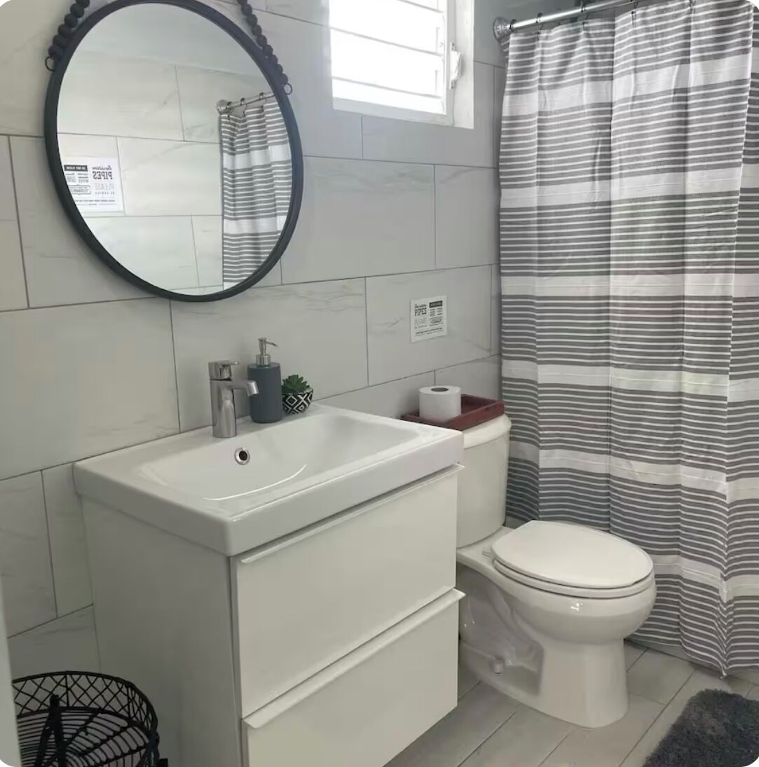 Ein Badezimmer mit einem weißen Waschbecken, einer Toilette, einem gestreiften Duschvorhang und einem Spiegel an der Wand.
