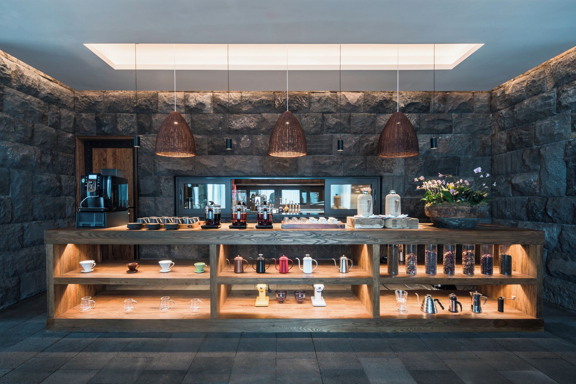 A bar area with a stone wall backdrop, multiple hanging pendant lights, and a variety of tea and coffee dispensers.