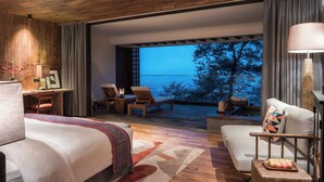 Un hotel moderno con una cama grande, una zona de estar con sillas, una mesita y vistas al mar.