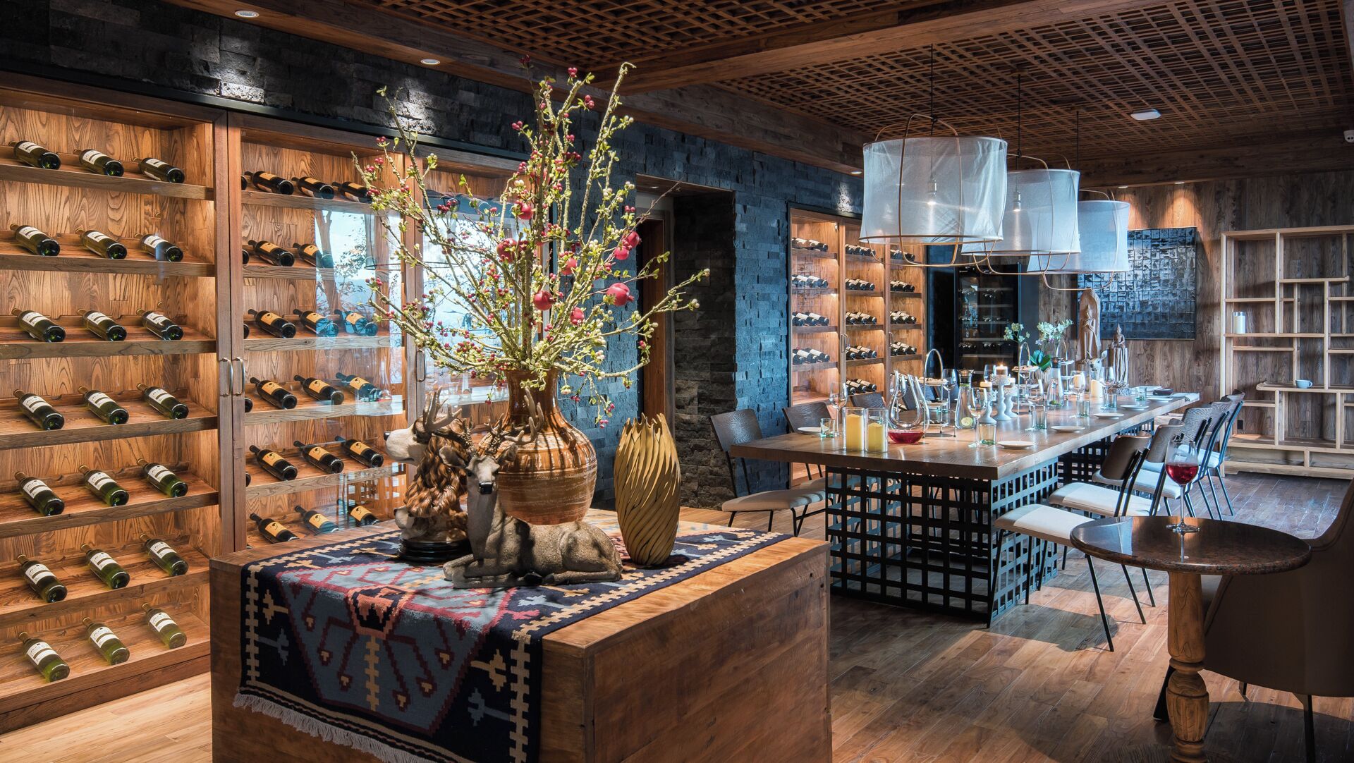 A modern bar area with wooden shelves displaying wine bottles, a central bar counter, and a seating area with chairs.