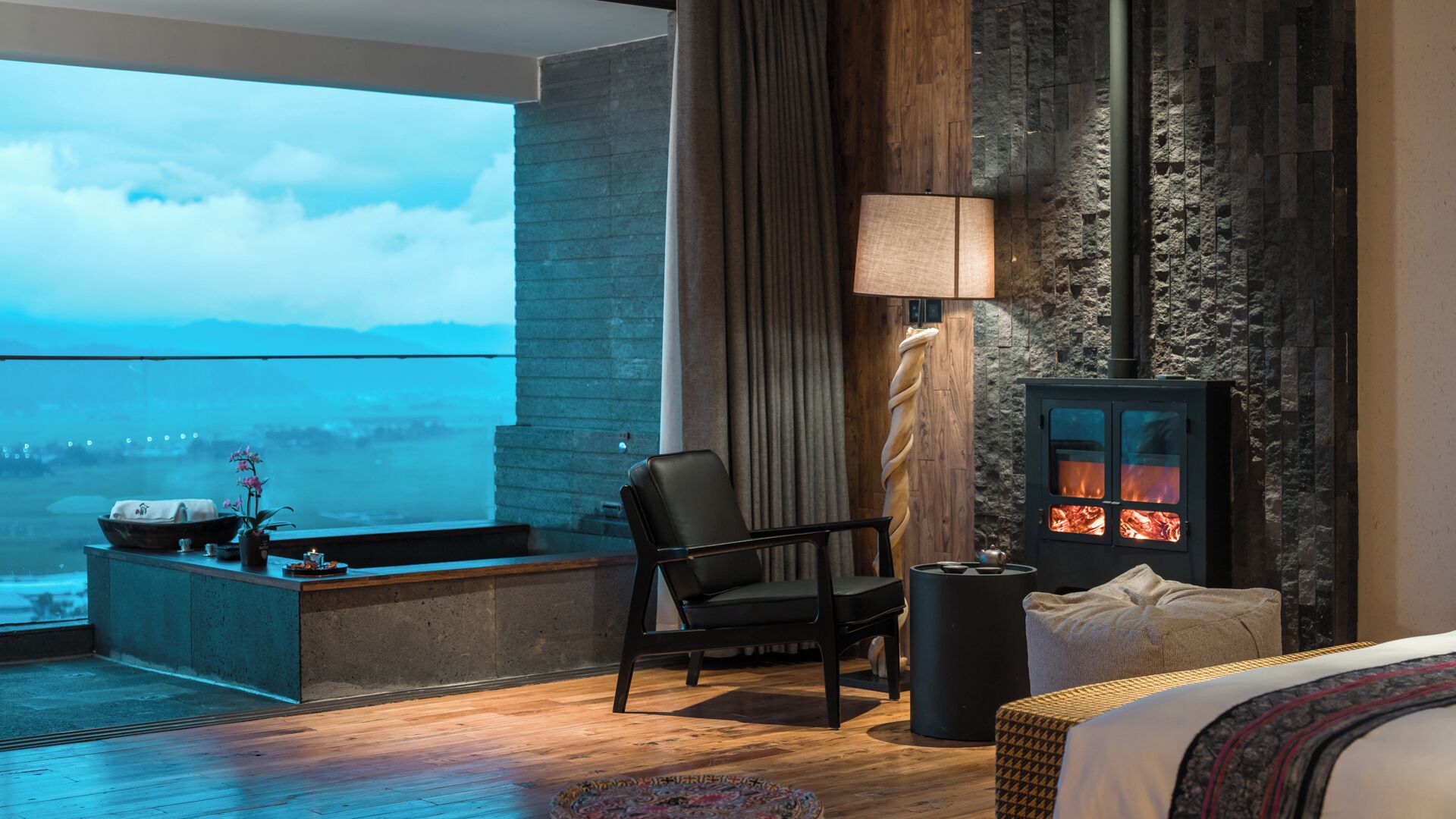 Ein modernes Hotelzimmer mit großem Fenster, Kamin, Schreibtisch und gemütlicher Sitzecke.