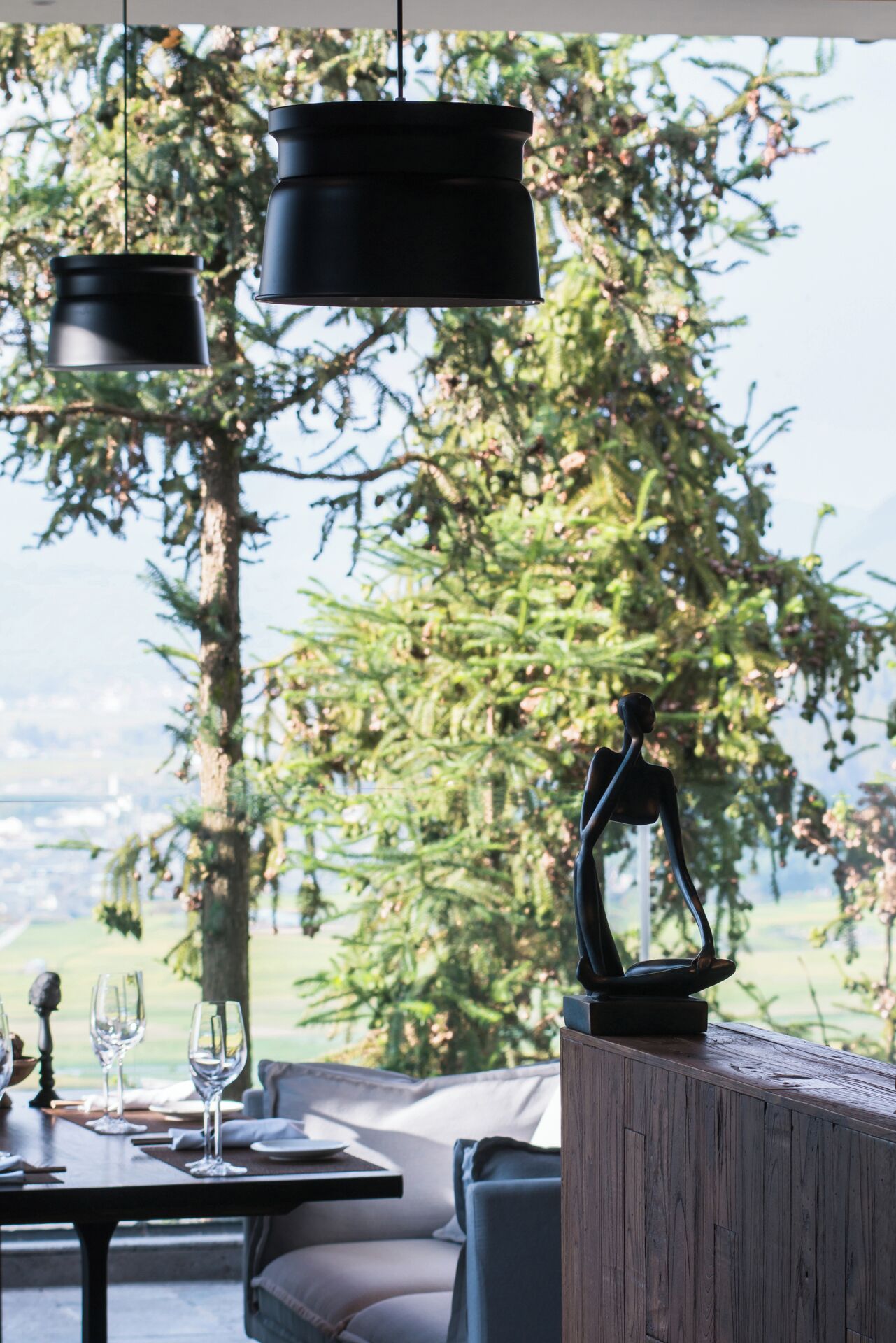 An outdoor dining area with a table set for two, a wooden bench, and a sculpture.