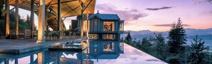 Una casa moderna con fachada de vidrio, terraza de madera y una piscina que refleja el entorno.