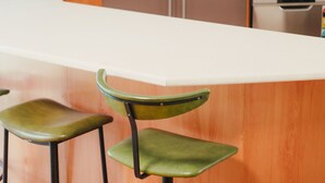 Una cocina moderna con armarios de madera, una encimera blanca y un microondas. Hay dos taburetes verdes en primer plano.