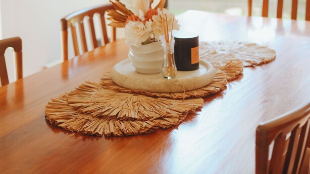 Una mesa de madera con un jarrón blanco, una vela negra y un mantel tejido.