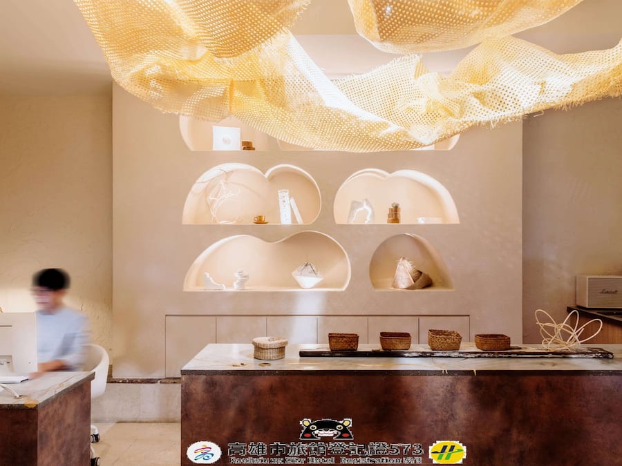 A hotel reception area with a modern design, featuring a reception desk, a digital display, and a decorative hanging light fixture.