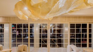 Un moderno vestíbulo de hotel con una amplia puerta de cristal, una zona de estar con sofás y una mesita, e instalación artística en el techo.