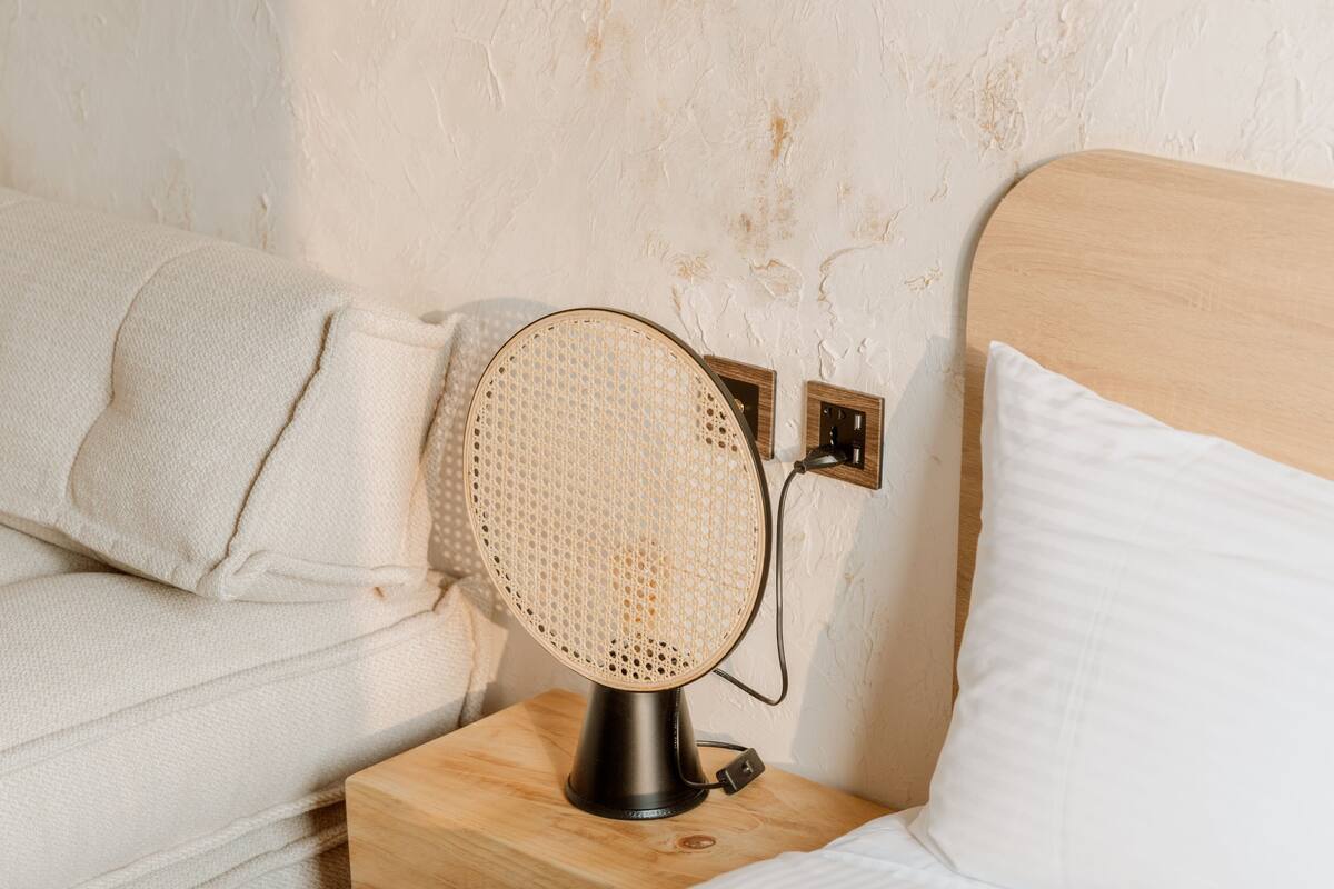 A bed with a white headboard, a wooden nightstand with a black lamp, and a textured wall.