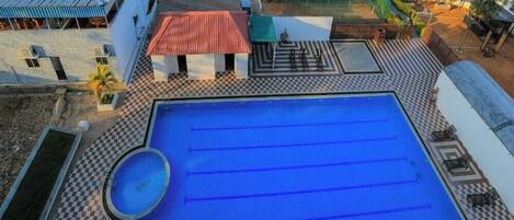 Una piscina en la azotea con suelo a cuadros, rodeada de edificios y una zona vallada.