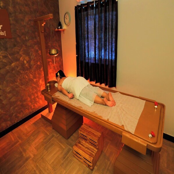 A massage table in a room with a wooden floor, a clock on the wall, and a window with curtains. - Exotic Retreat (Gorentla)