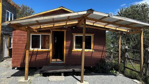 A small wooden house with a porch, a front door, and two windows. - Mateo Puyuhuapi Cabin (Puyuhuapi)