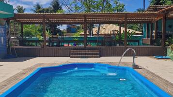 A rectangular swimming pool with clear blue water, surrounded by a wooden deck and a covered seating area.