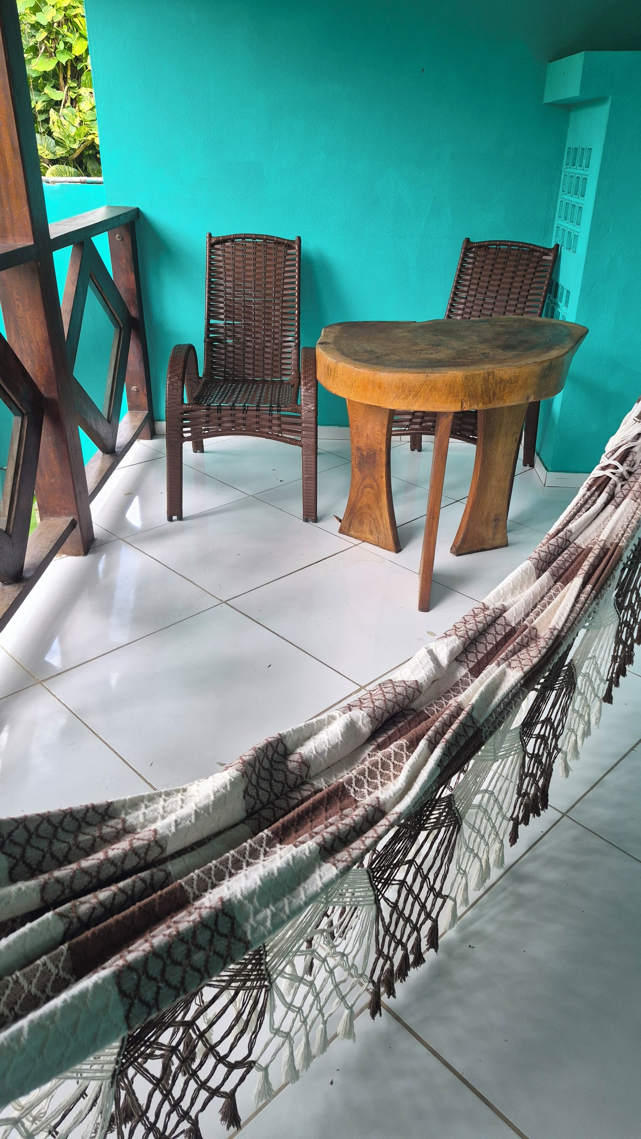 A room with a wooden table and two wicker chairs, a hammock, and a turquoise wall.