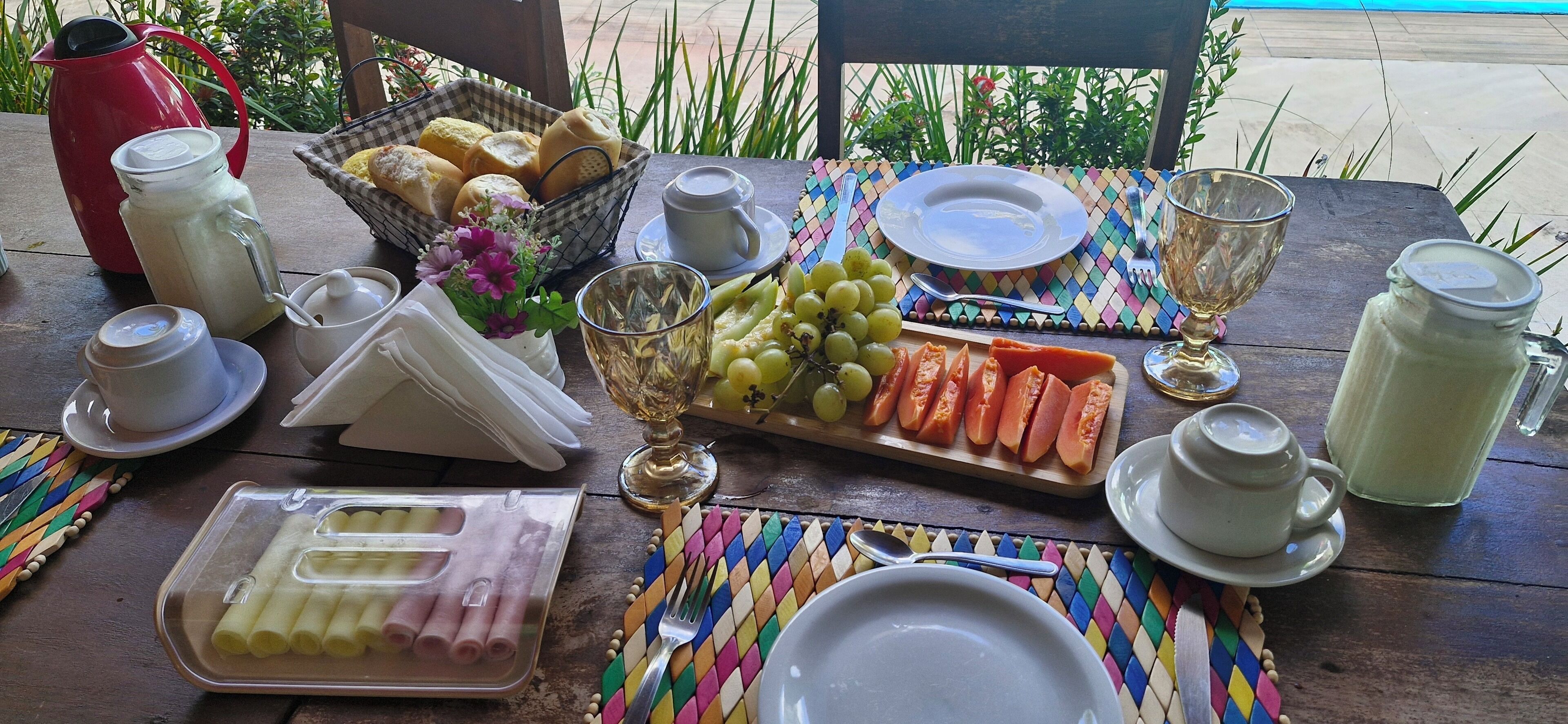A table set with various food items, including bread, grapes, and sliced vegetables, along with multiple cups and a pitcher.