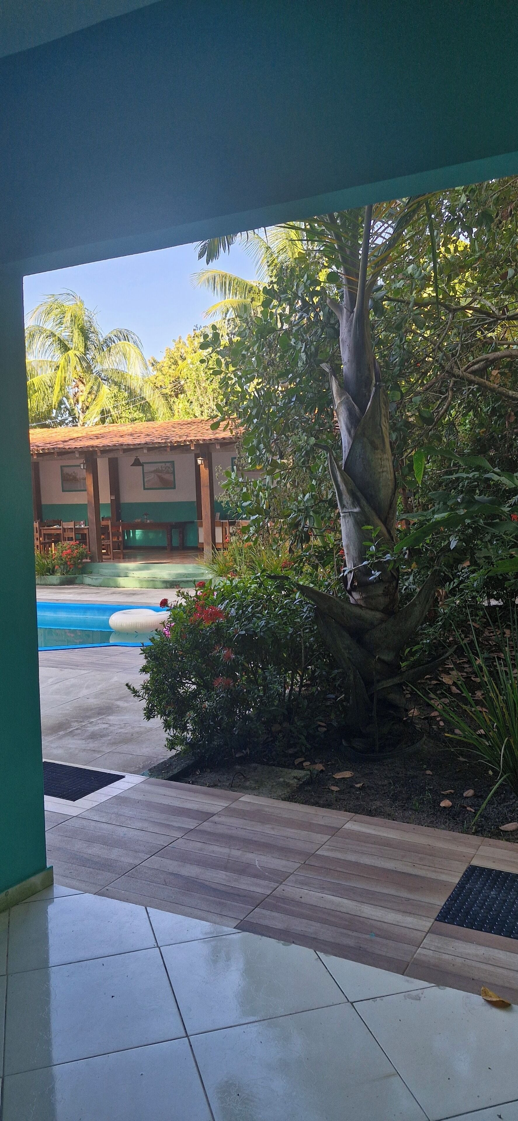 Blick auf einen Poolbereich mit einer Statue, umgeben von Grünpflanzen und einem Gebäude mit einem Ziegeldach.