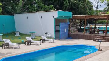 Una piscina con solárium empedrado, rodeada de sillones de descanso y un área de estar cubierta.