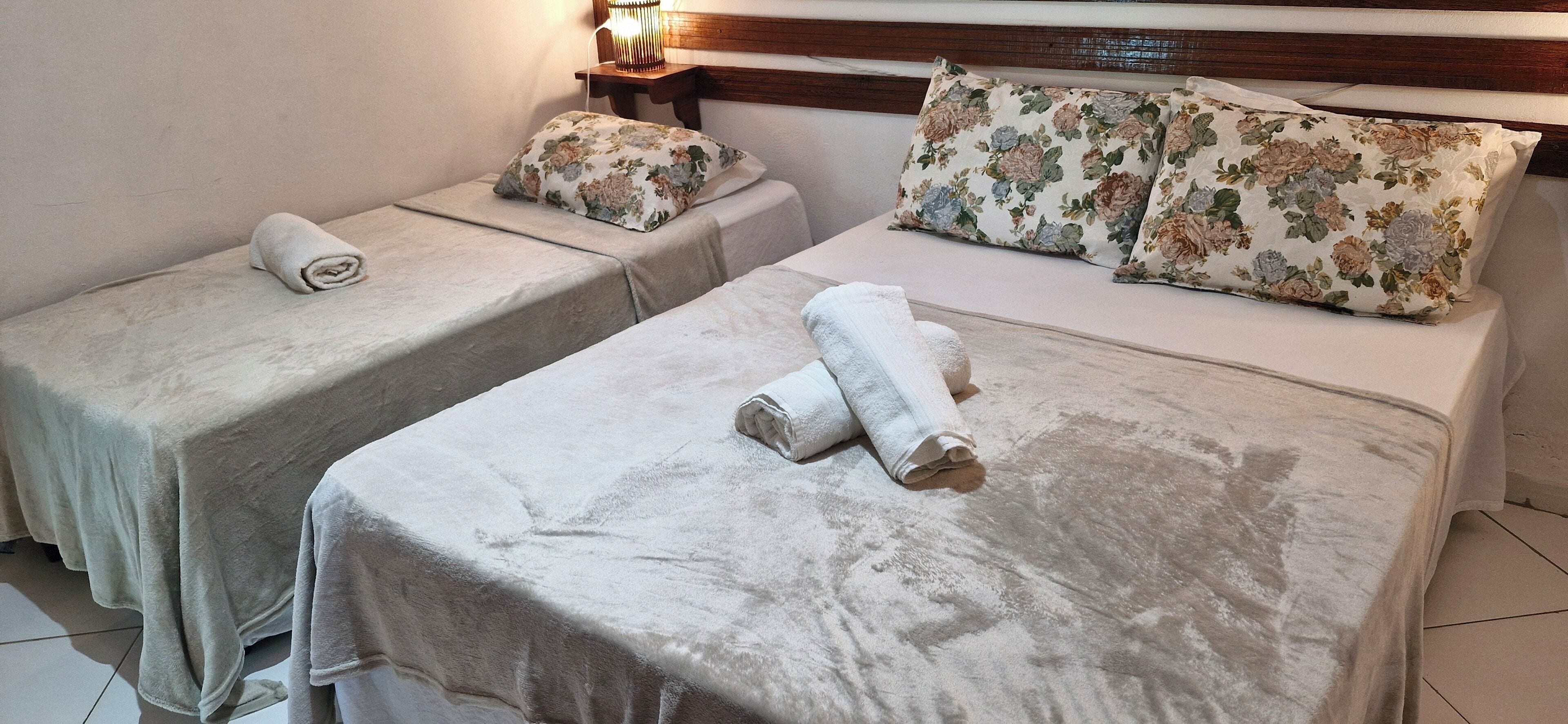Two twin beds with floral bedding and towels, a bedside table with a lamp, and a wooden headboard.