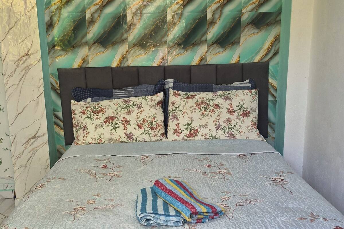A bed with a floral bedspread, a striped blanket, and a headboard with a marble-like pattern.