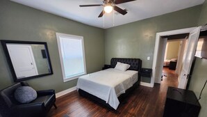 A bedroom with a bed, a chair, a desk, a ceiling fan, and a door leading to another room. - Charming 2 BR retreat in Shreveport, minutes from Casinos, airport & attractions (Shreveport)