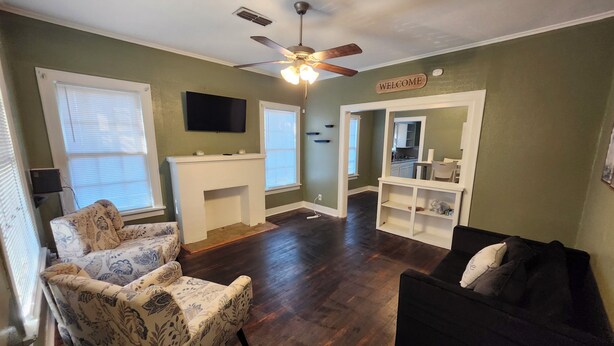 A living room with a fireplace, a ceiling fan, a TV mounted on the wall, and a 'WELCOME' sign. - Charming 2 BR retreat in Shreveport, minutes from Casinos, airport & attractions (Shreveport)