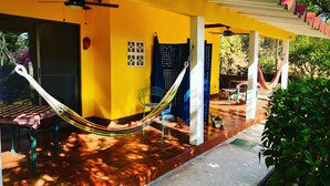 Un bâtiment jaune avec une terrasse carrelée, un hamac et un ventilateur de plafond.